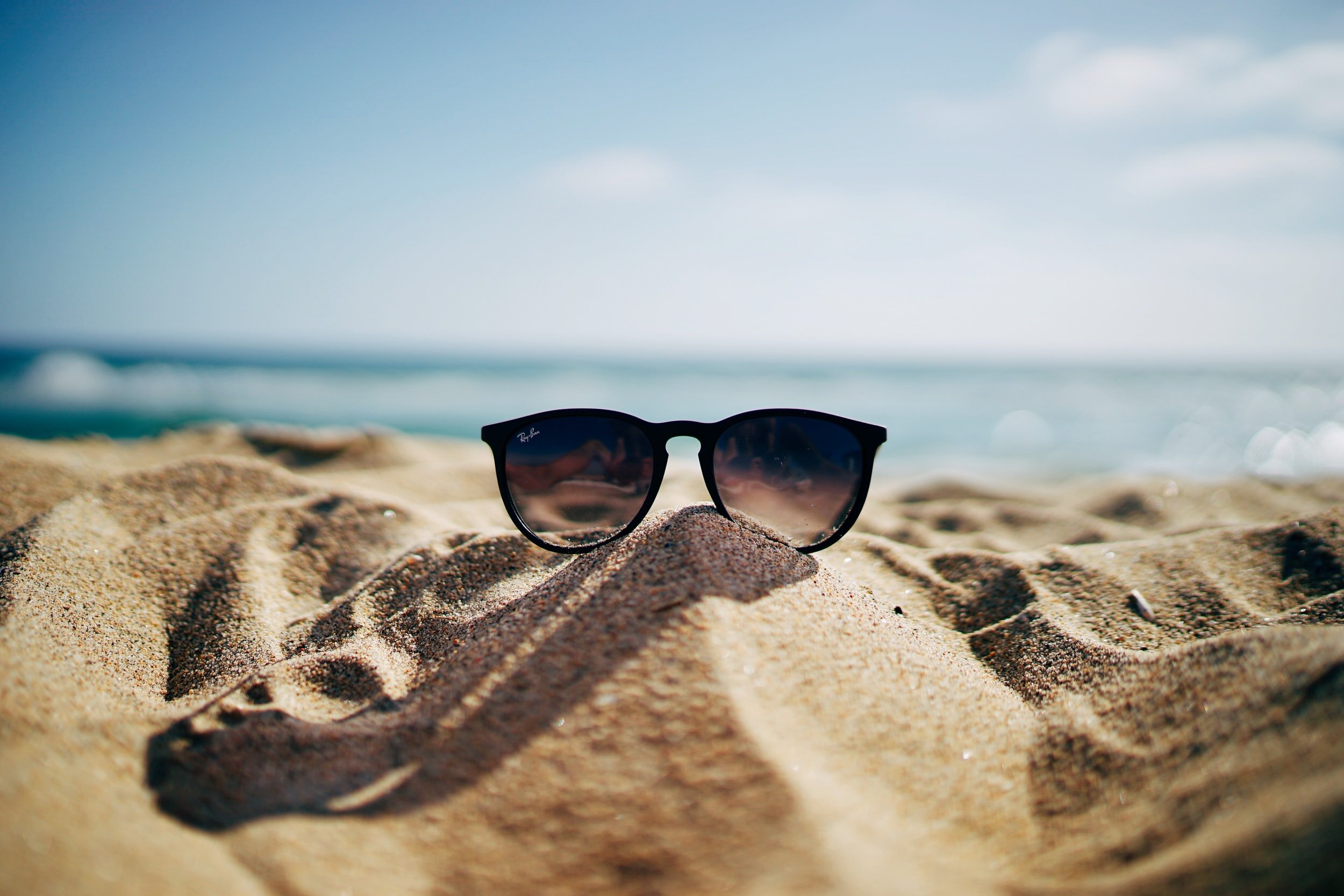 Photo by Ethan Robertson on Unsplash Photo of a pair of sunglasses witting in the sand. You can see the water behind them.