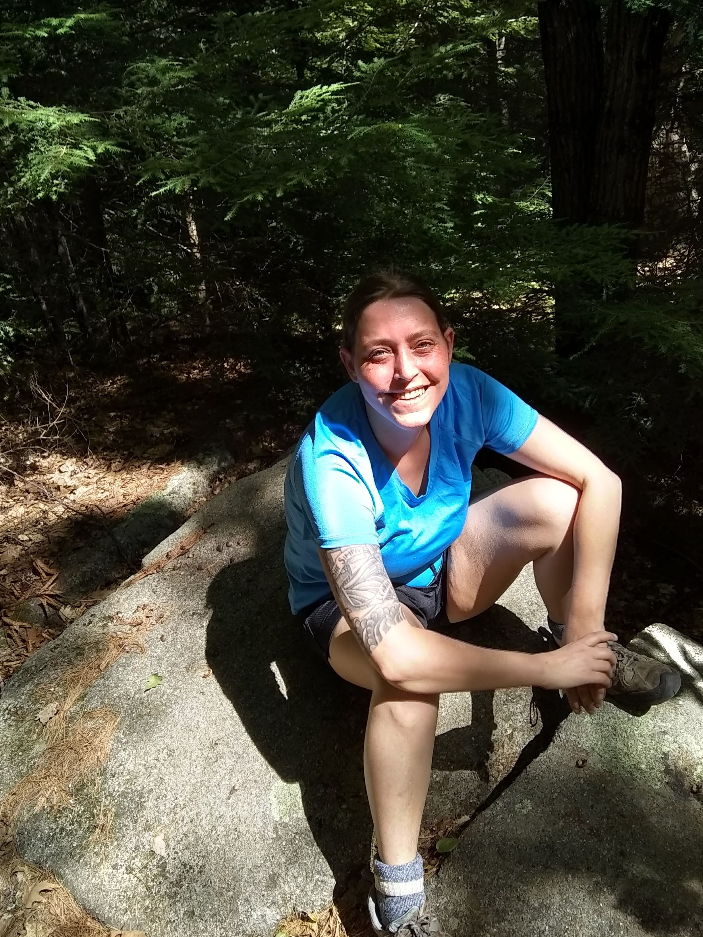 The blog authorized, a woman with brown hair sitting on a rock in the woods.