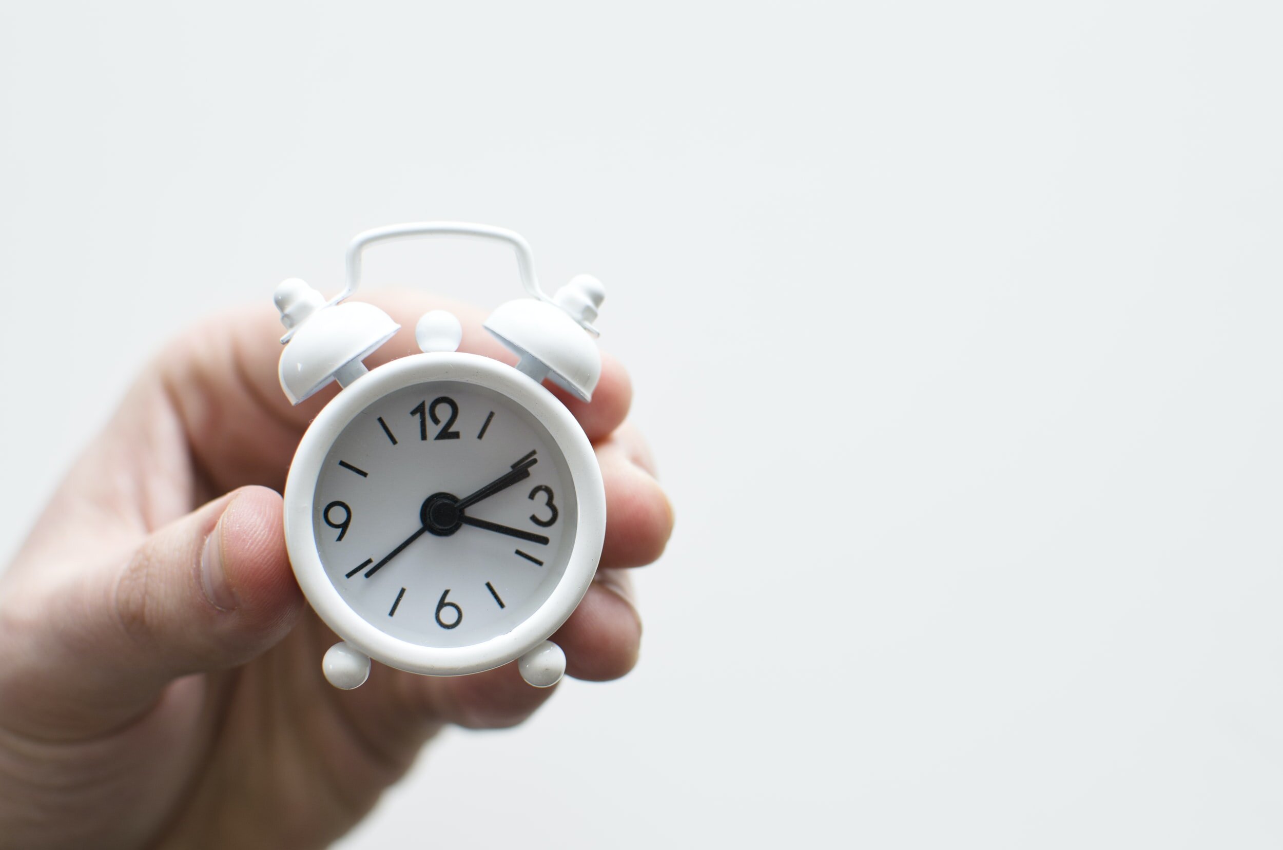 Photo by Lukas Blazek on UnsplashA person holds up a little white clock. There is a white background