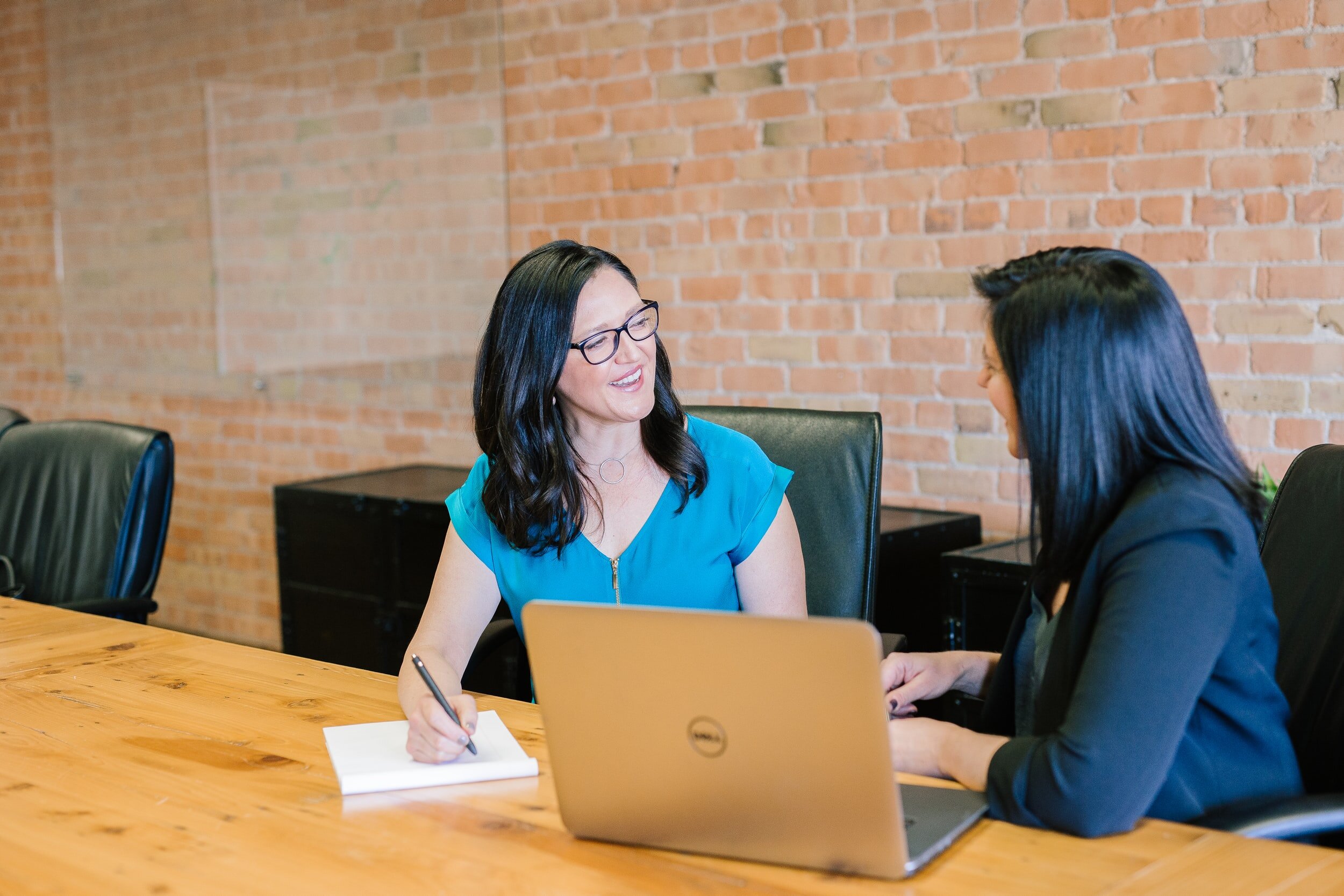 Photo by Amy Hirschi on Unsplash Two people speak at a table with a laptop in the center.