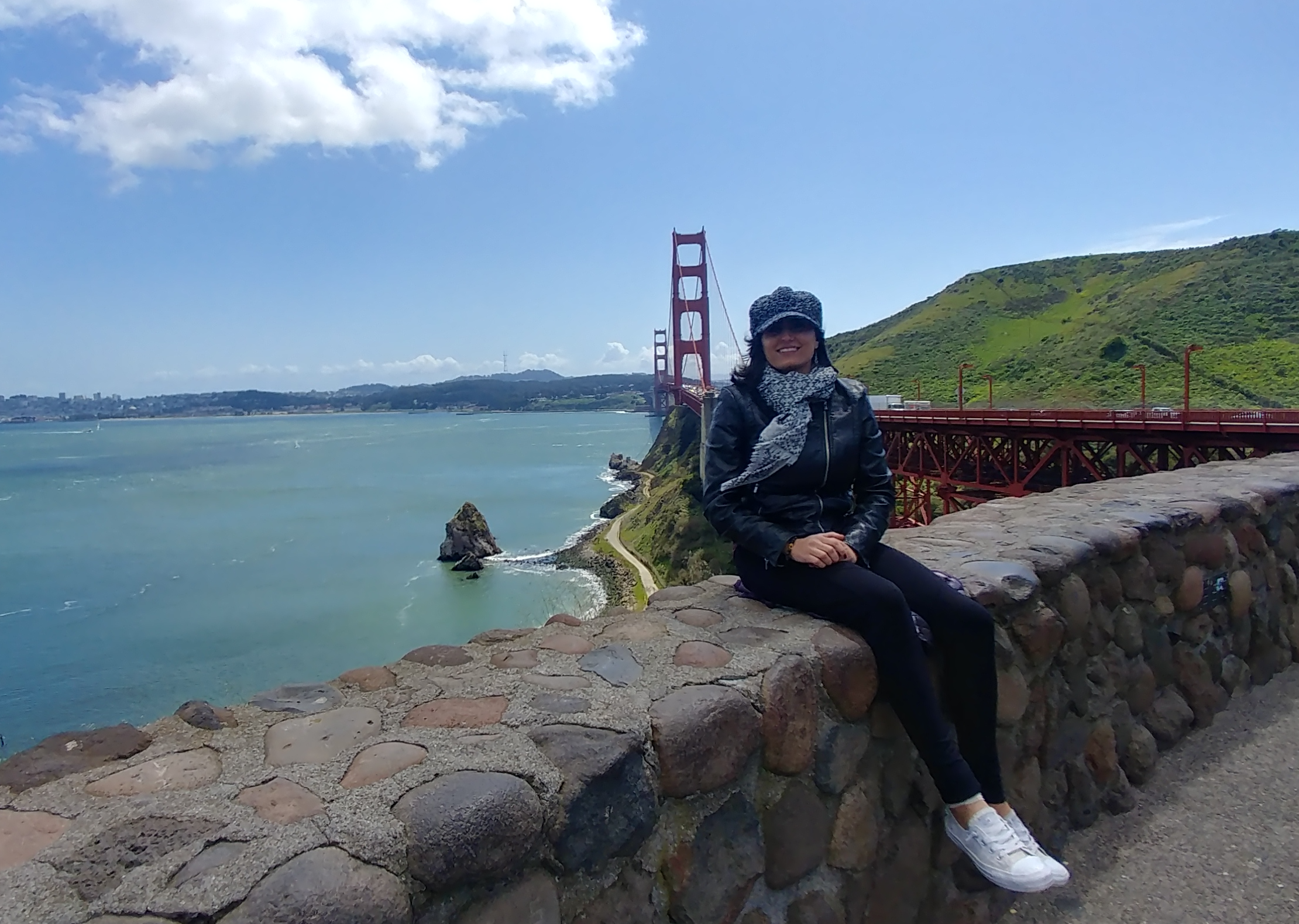 An image of the blog author, Tina sitting on a stonewall outside in front of a river and red bridge.