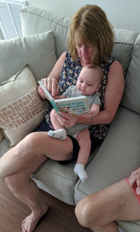 Photo of Annemarrie sitting on a couch and reading to an adorable baby!