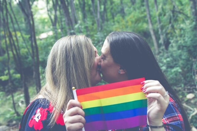 Image of the blog author kissing her wife holding a rainbow flag.