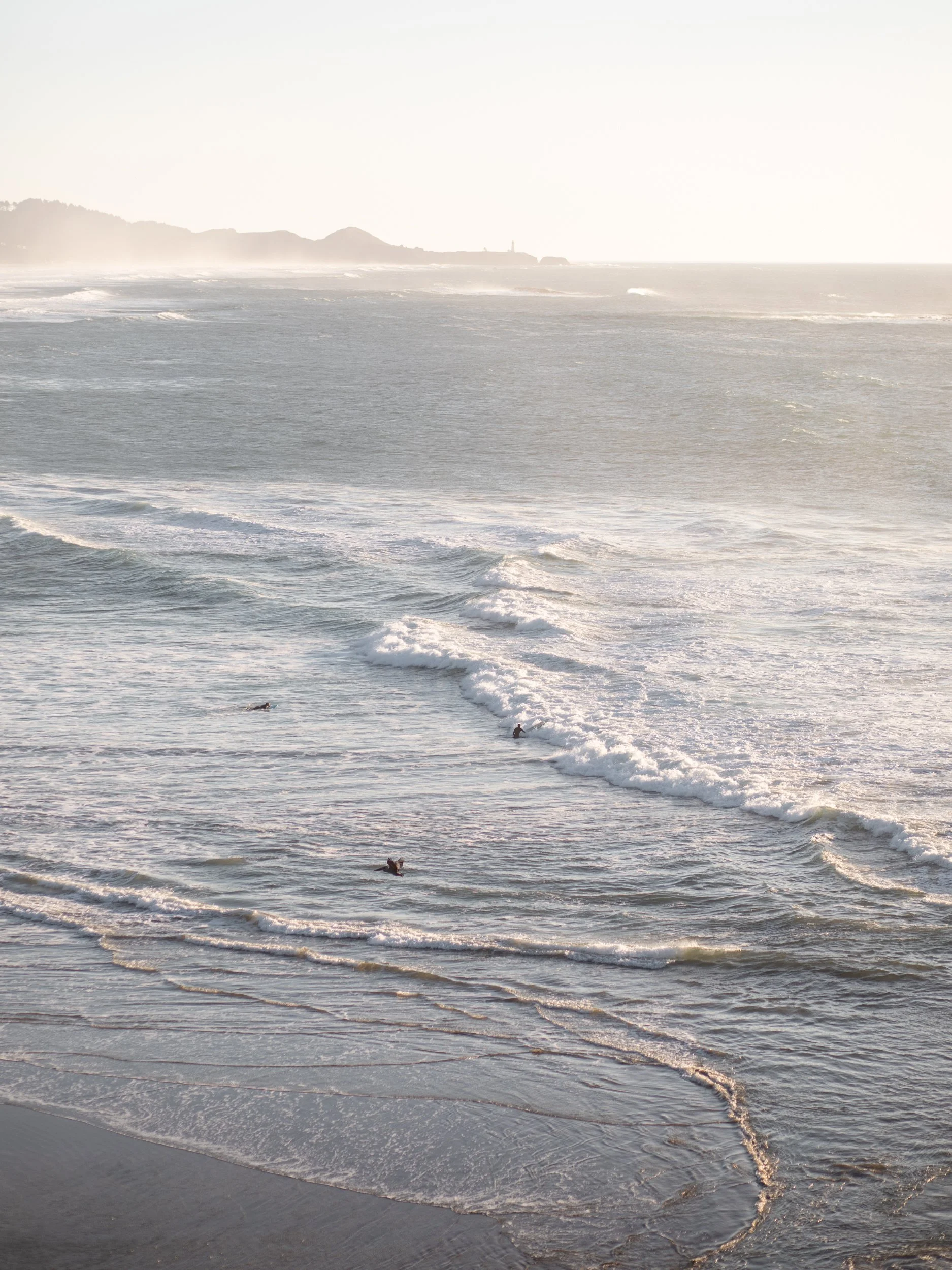 overlooking the Pacific ocean, surfers, and distant lighthouse at sunset