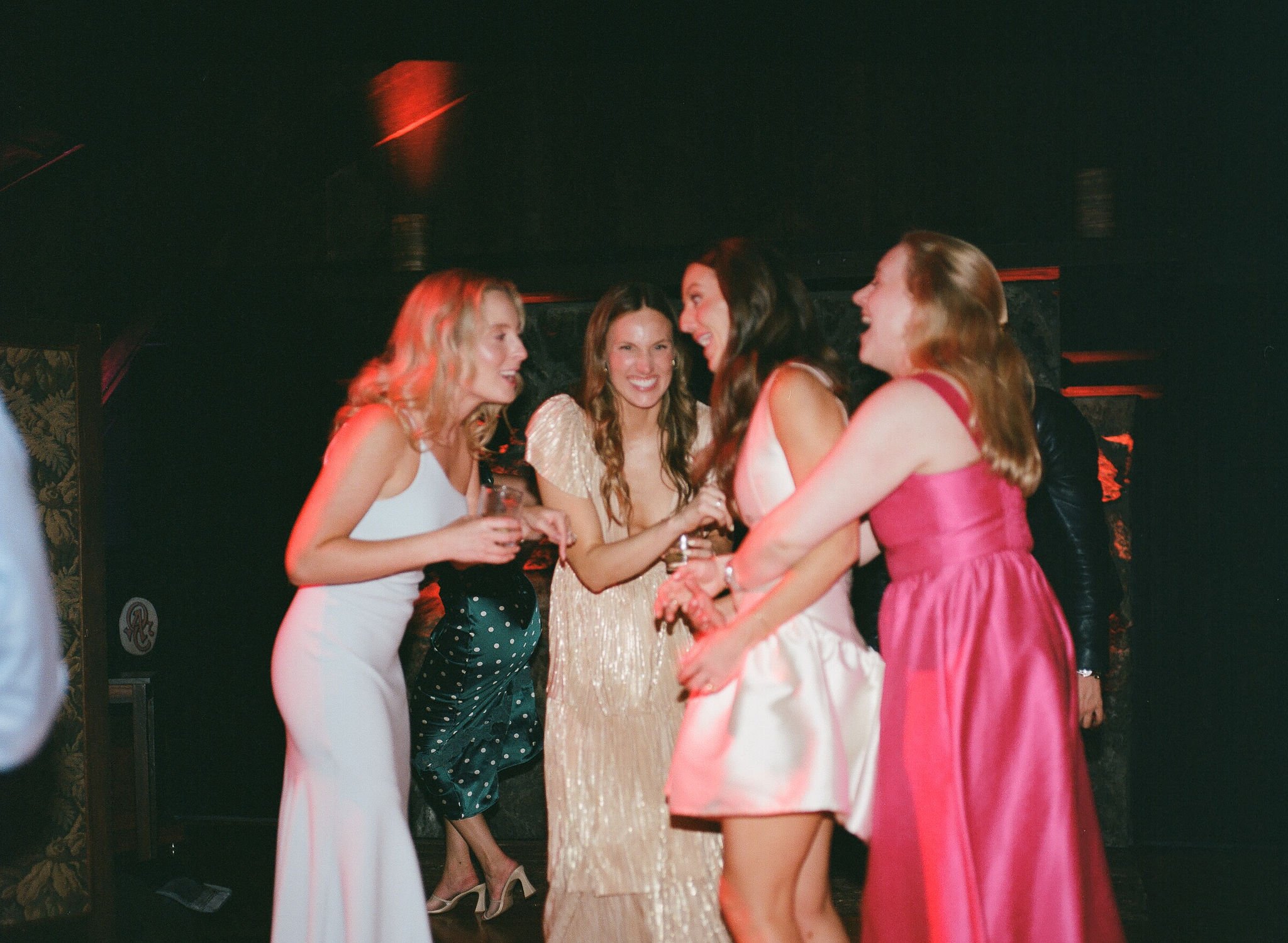 A film photo with flash of a group of women in glamorous dresses talking and laughing at a party or wedding celebration.
