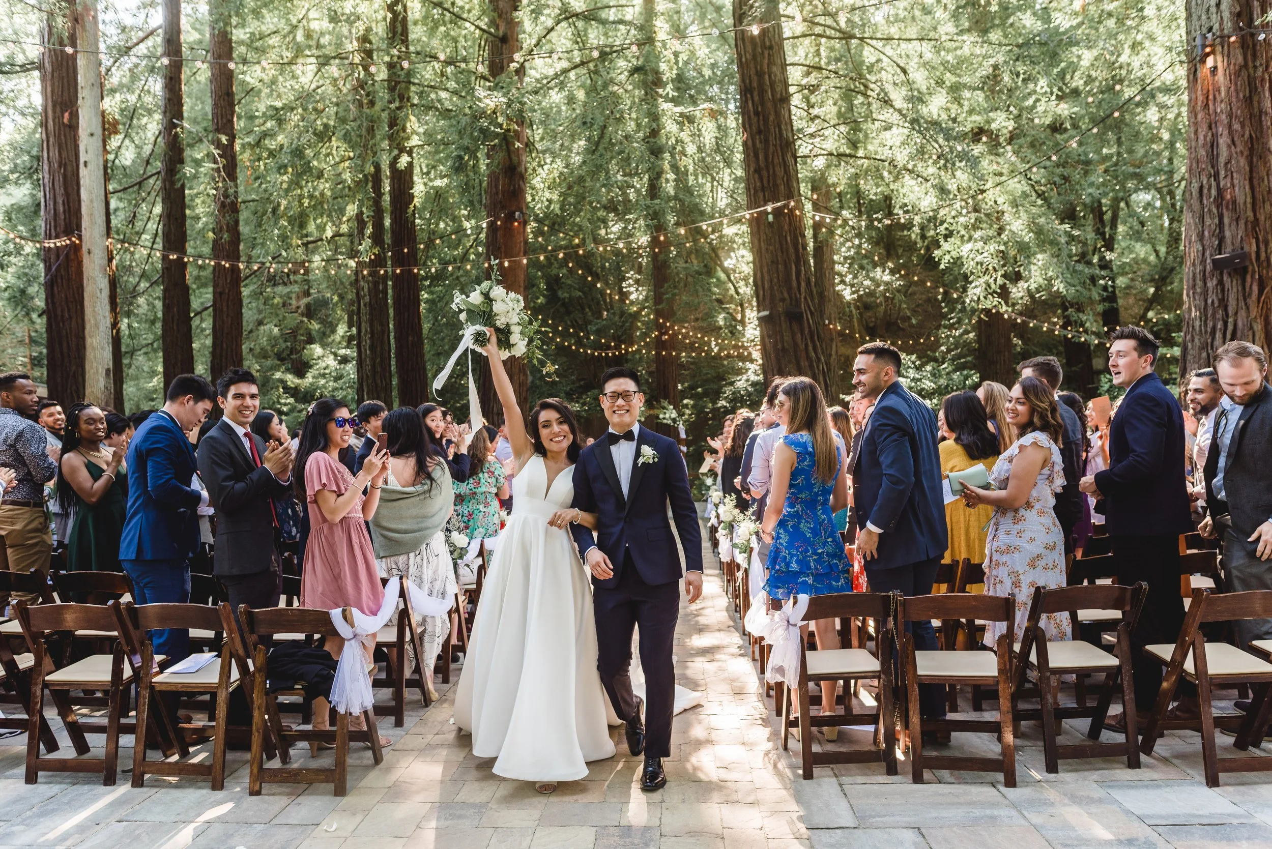 a bride and groom cheersing with her hands up holding her bouquet after saying yes and walking back down the aisle at deer park villa