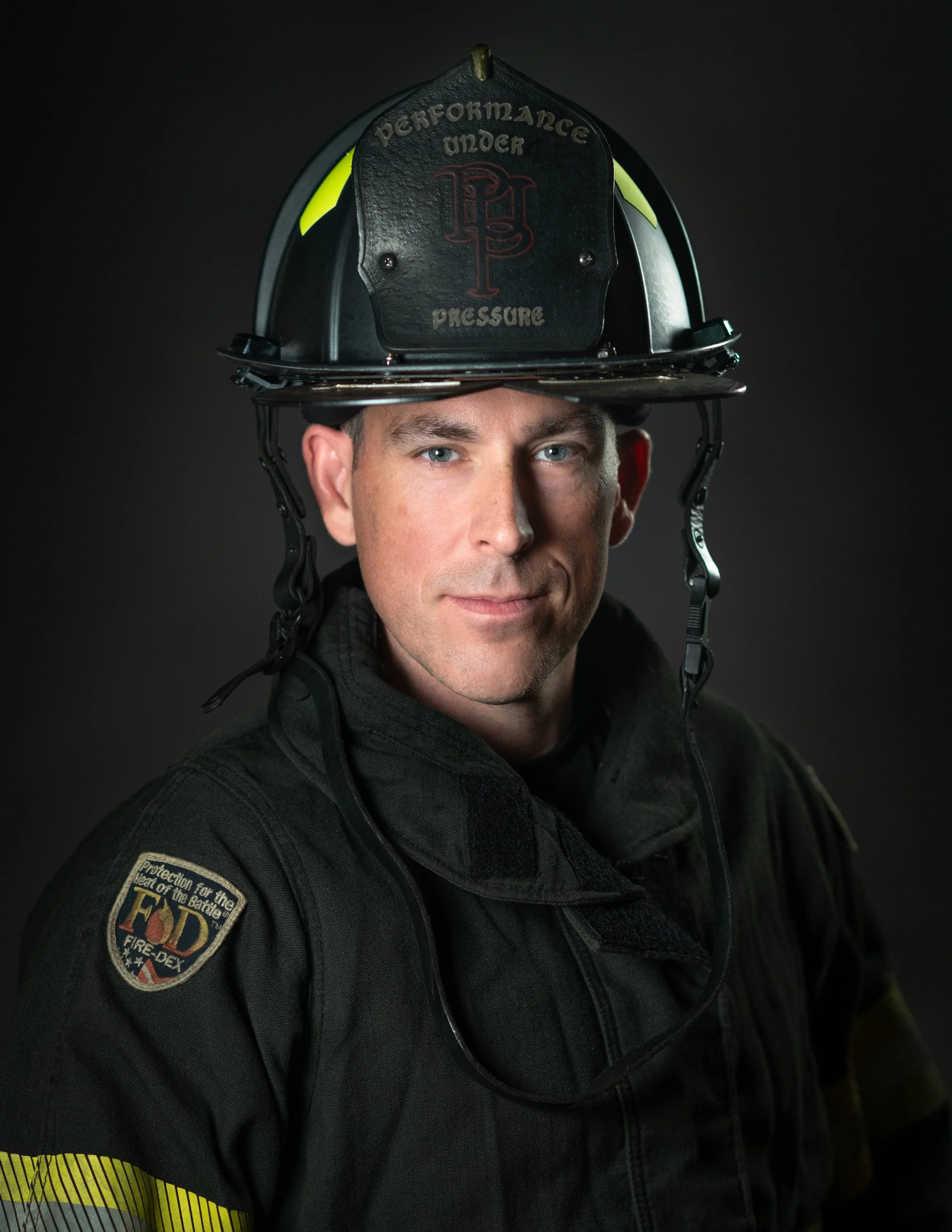 A firefighter in uniform wearing a black helmet, with reflective yellow patches, and a badge that reads 'Protection for the men and the battle'.