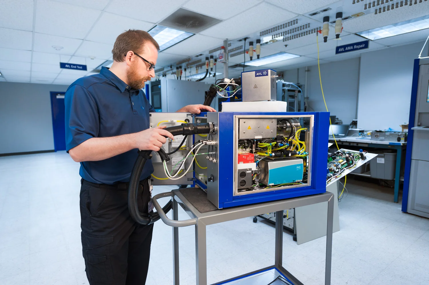 A technician working on a complex piece of equipment with wires and electronic components in a laboratory setting.