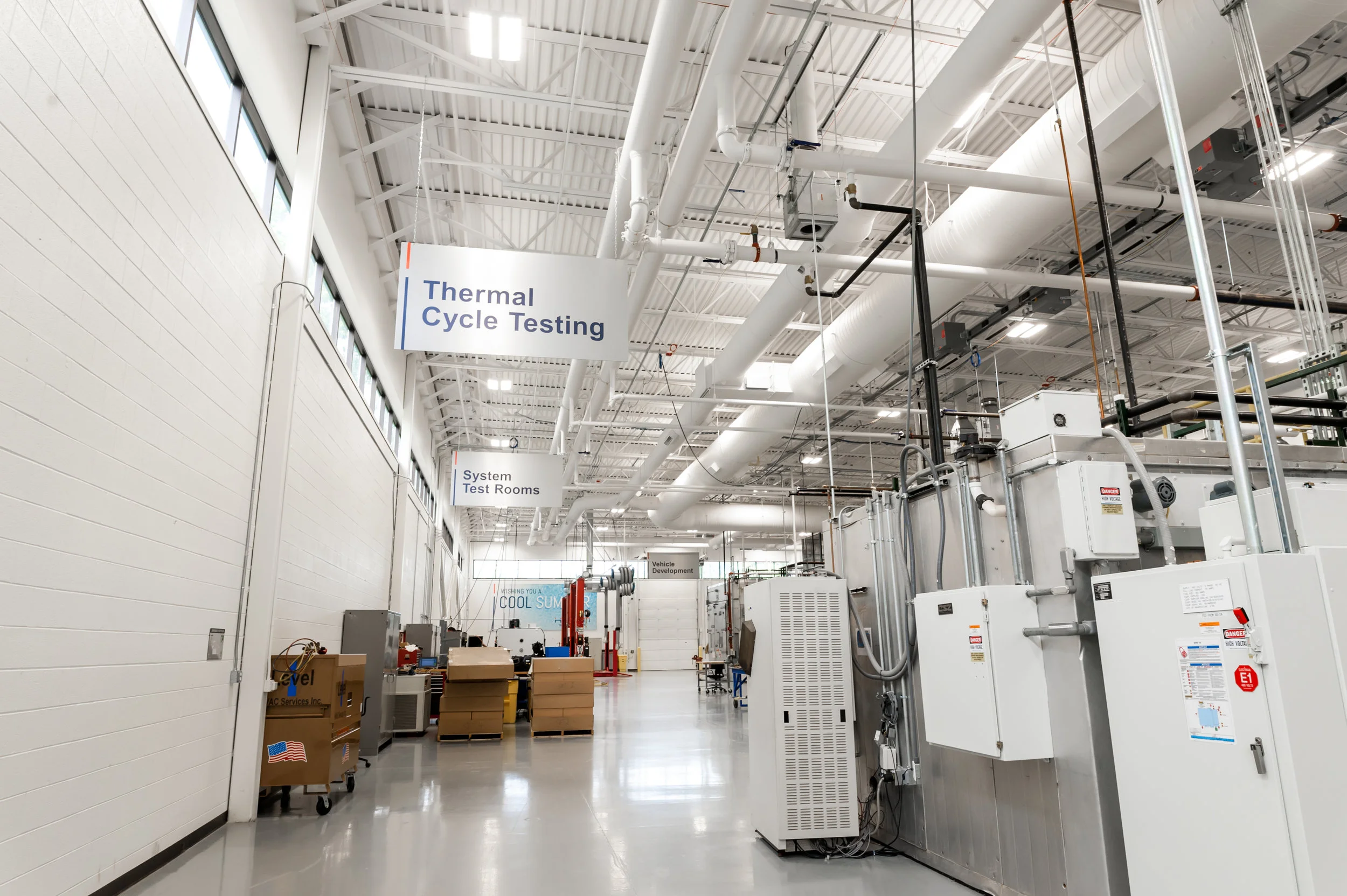 Interior of a testing facility with signs reading 'Thermal Cycle Testing' and 'System Test Rooms'; equipment and machinery used for testing are visible.