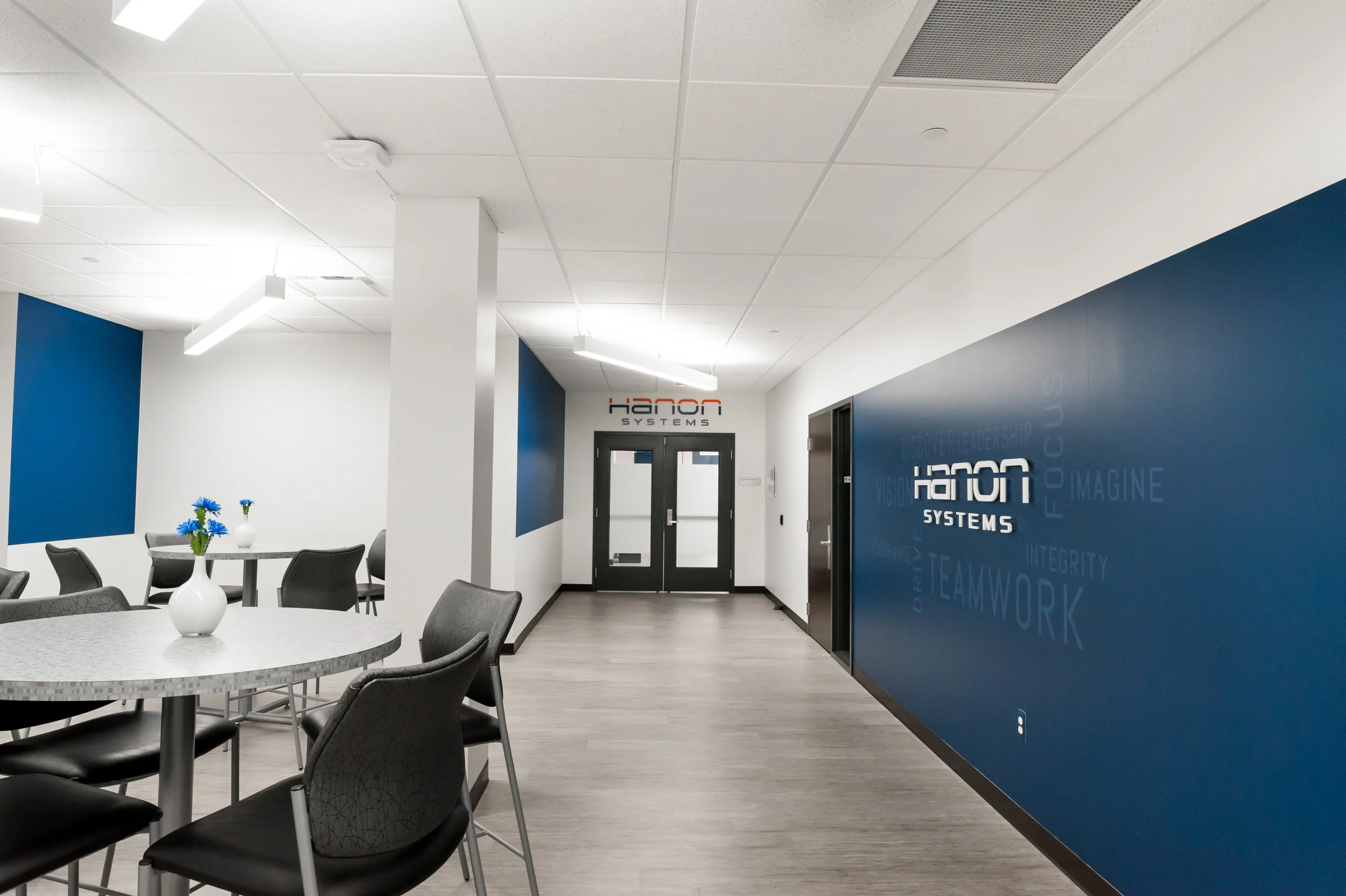 Modern office lobby with white and blue walls, round tables with black chairs, and a wall sign for Honor Systems.