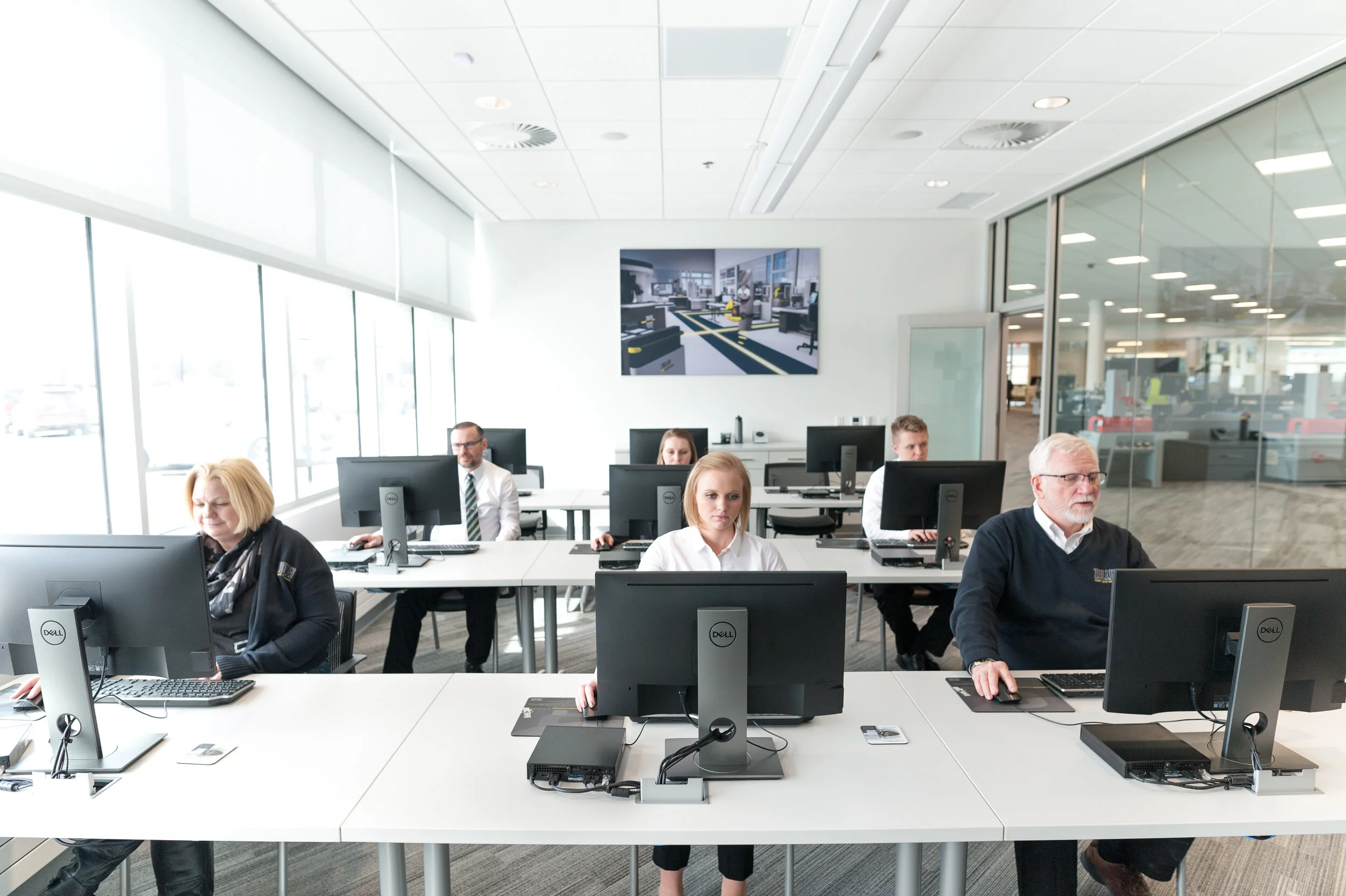 People working at computers in a modern office with large windows and a glass wall.