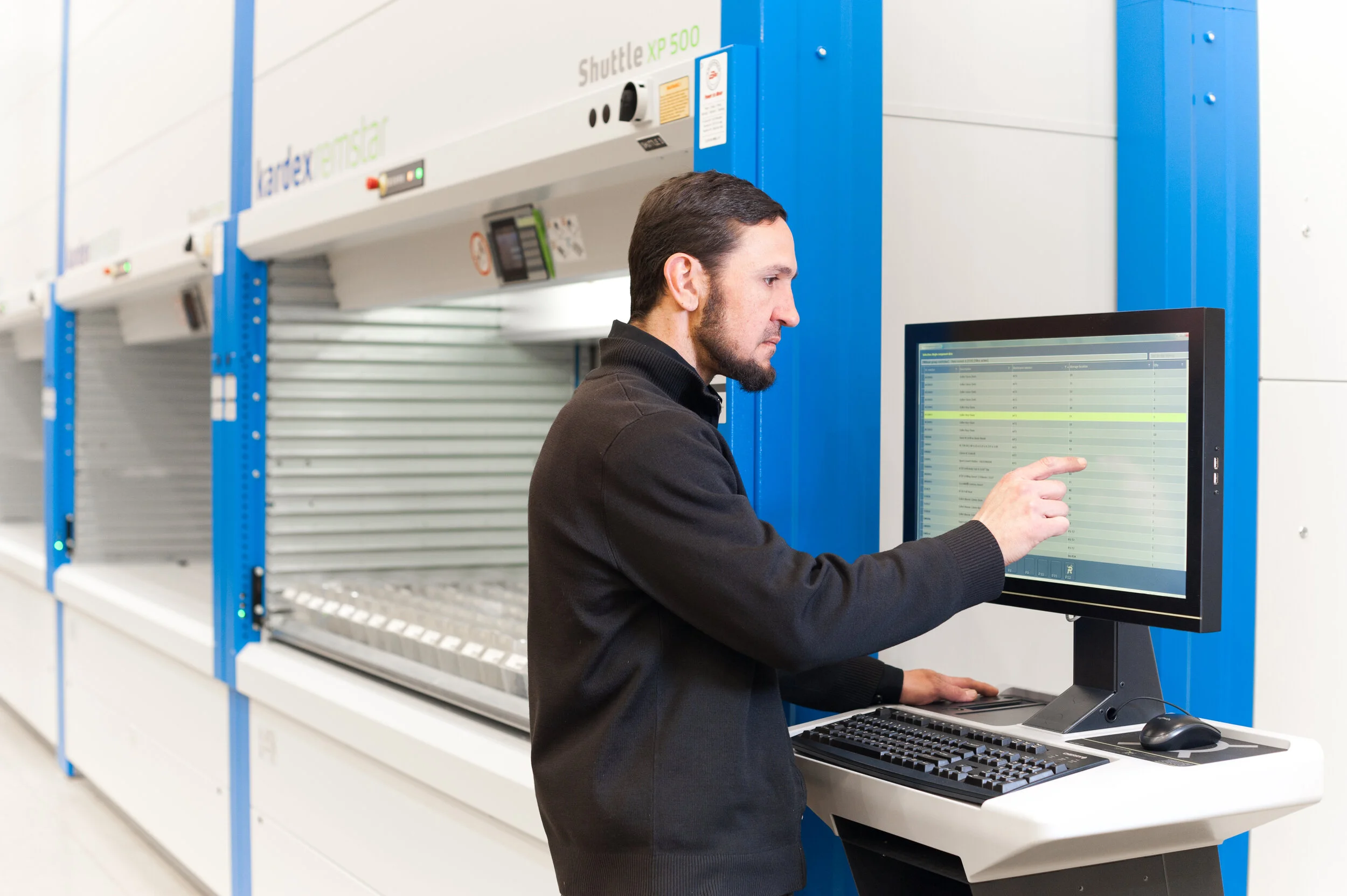A man in a black jacket operating a computer in front of high-tech equipment in a laboratory or data center.