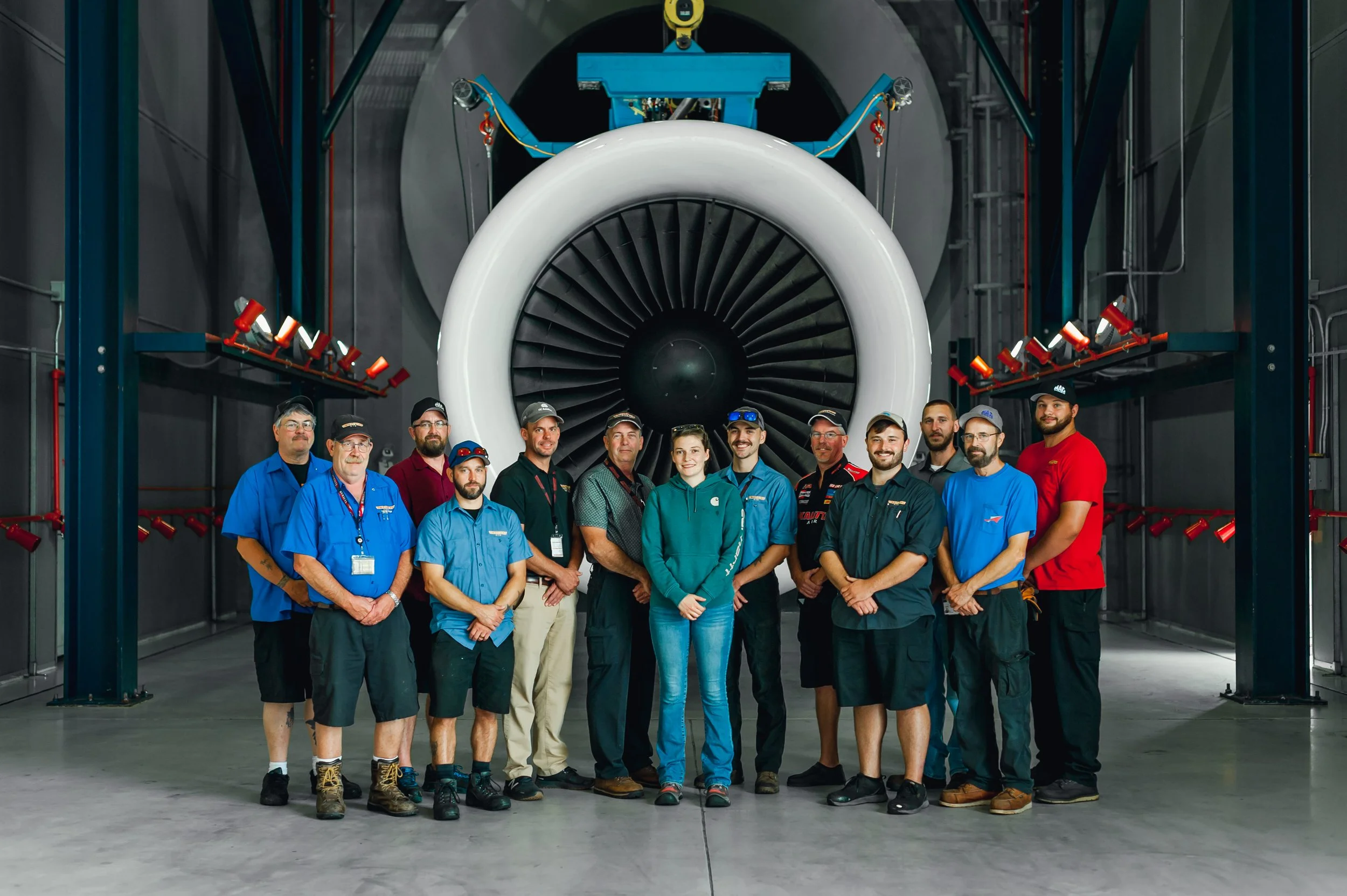 Group of people standing in front of a large aircraft engine inside an aerospace facility.