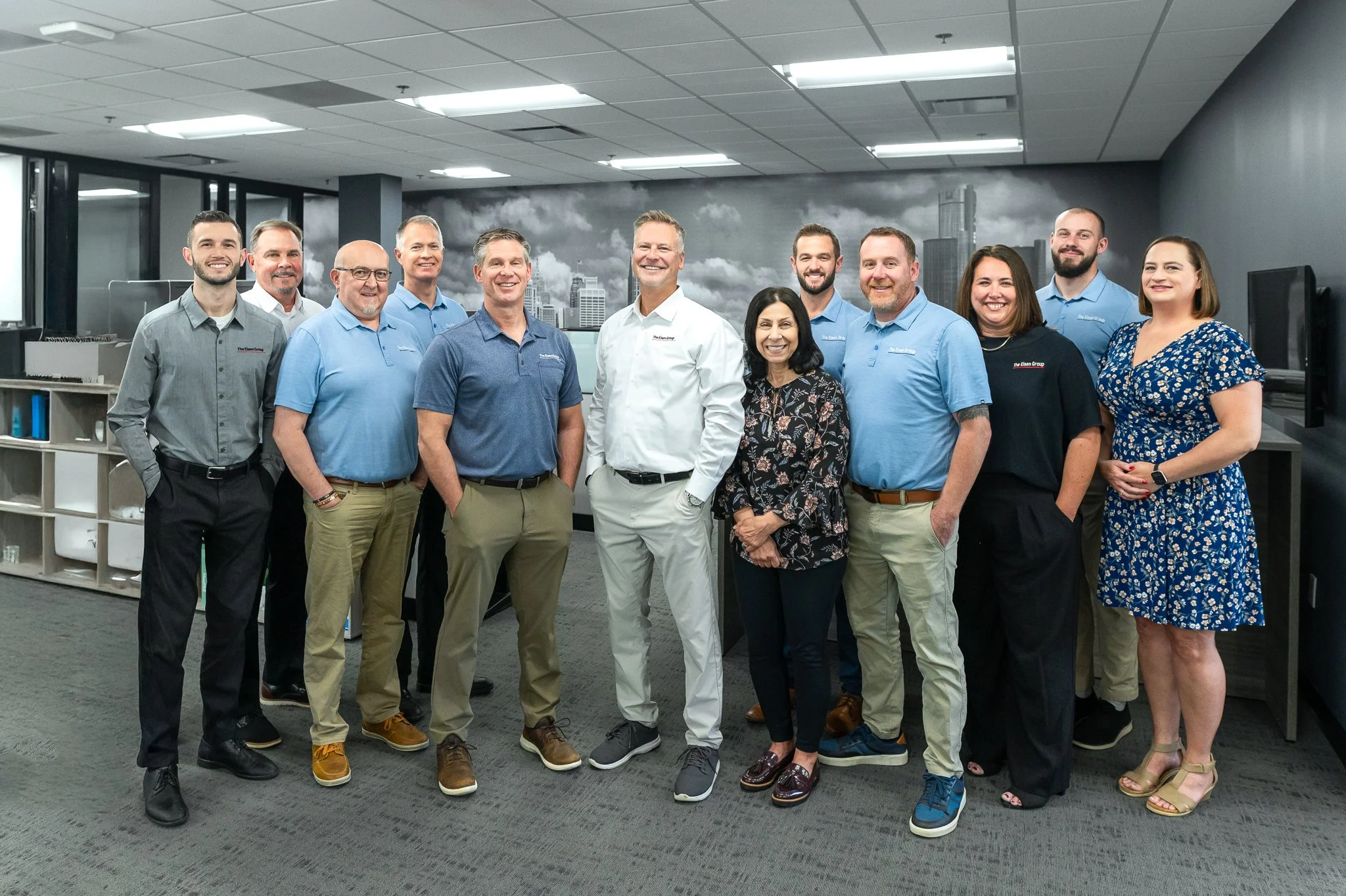 Group of diverse professionals posing indoors with a cityscape mural in the background.