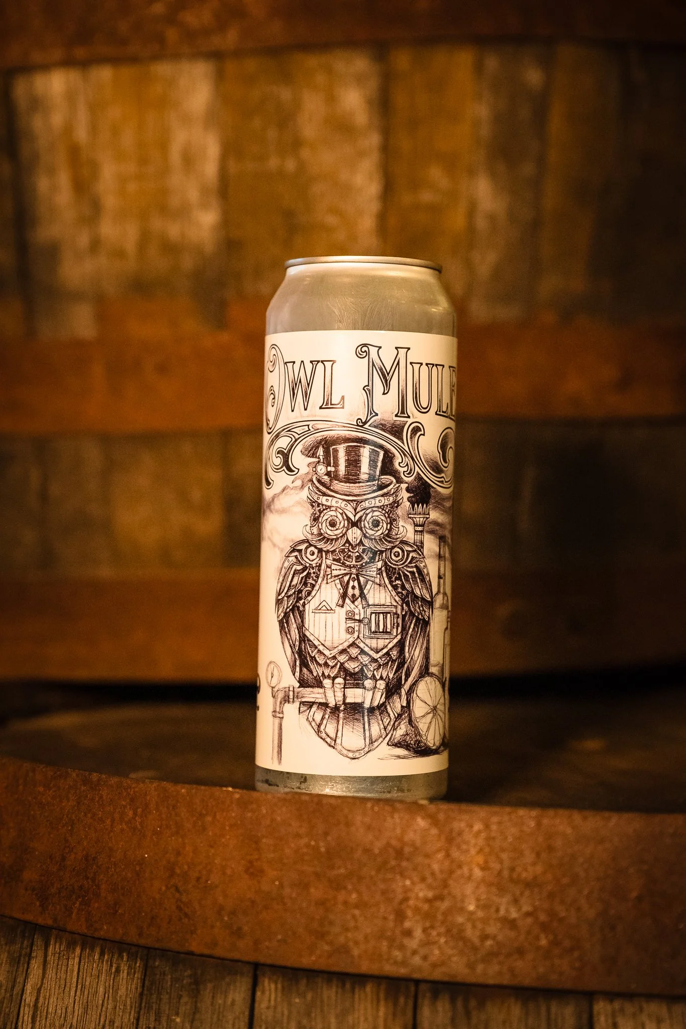 A tall silver can with black and white illustration of an owl wearing a top hat and bow tie, holding a paintbrush and standing in front of a window, with the words 'OWL MULE' on the label.