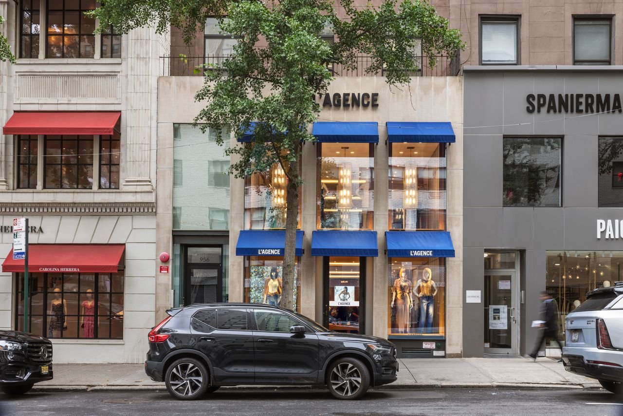 Street view of the L'AGENCE flagship boutique on Madison Avenue in New York City, designed by Paul Bennett Architects, featuring a limestone façade, blue awnings, and storefront windows within the surrounding luxury retail district.