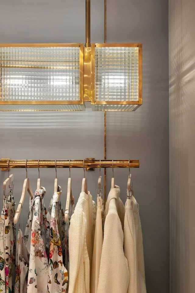 Detail of a custom brass clothing rail and textured glass pendant light inside the L'AGENCE flagship boutique, highlighting the refined material palette and residential-inspired retail design by Paul Bennett Architects.