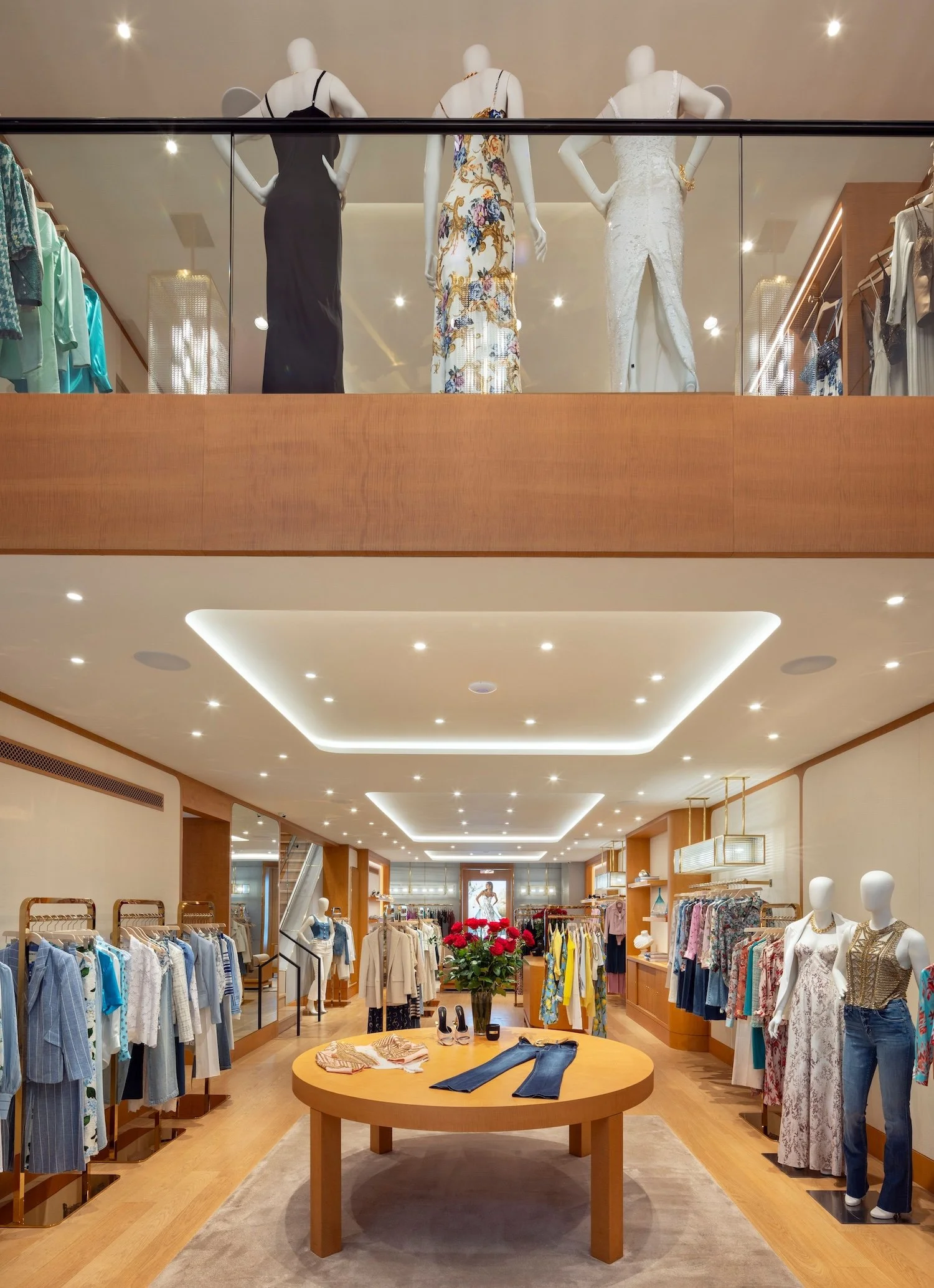Two-story interior of the L'AGENCE flagship boutique in New York City, featuring custom wood millwork, open mezzanine, curated retail displays, and warm residential-inspired design by Paul Bennett Architects.