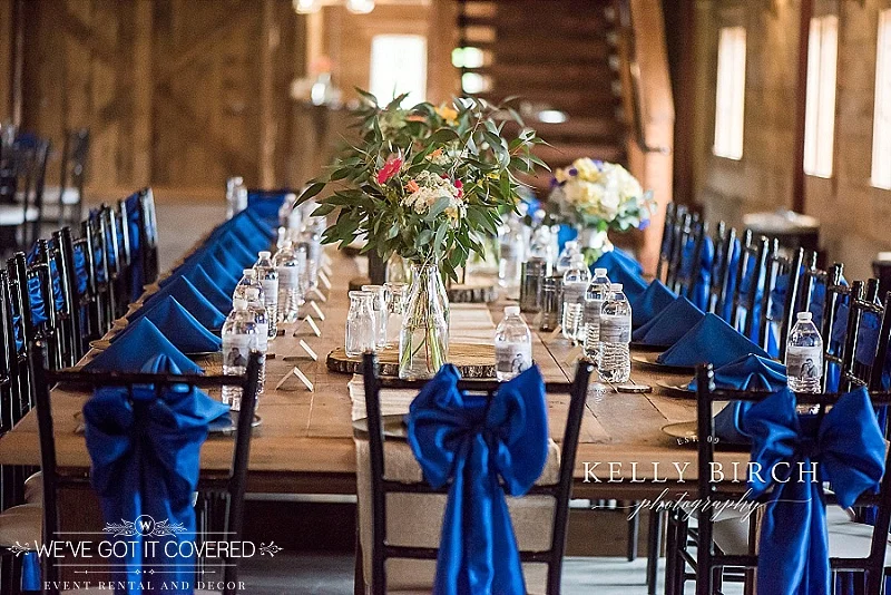 Head table with satin sashes tied in a bow and wood slice centerpieces with flowers.