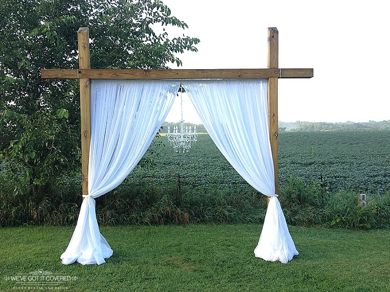 Farm venue arch with white curtain draping and a crystal chandelier hung in the middle of a field