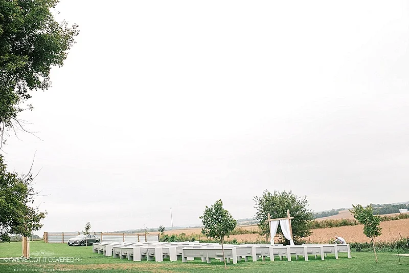 Ceremony site with outdoor pews and trees and draping on the ceremony arch.