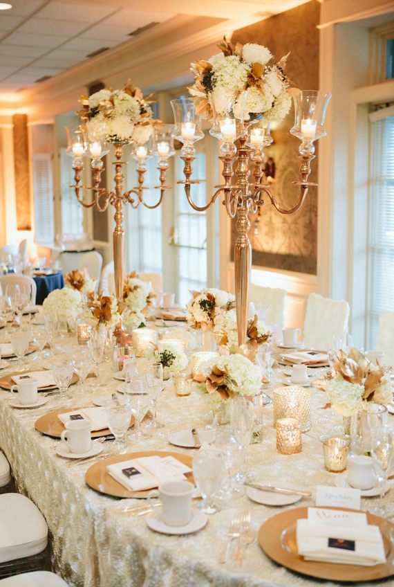 Harvest table with a rosette linen, gold chargers, variety of candle holders, tall floral plates and navy accents.