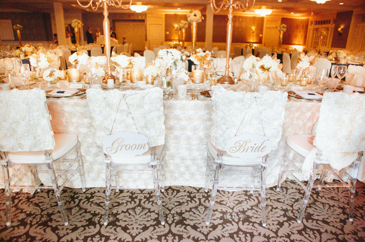 Bride and groom chairs with rosette flower linens and gold accents throughout