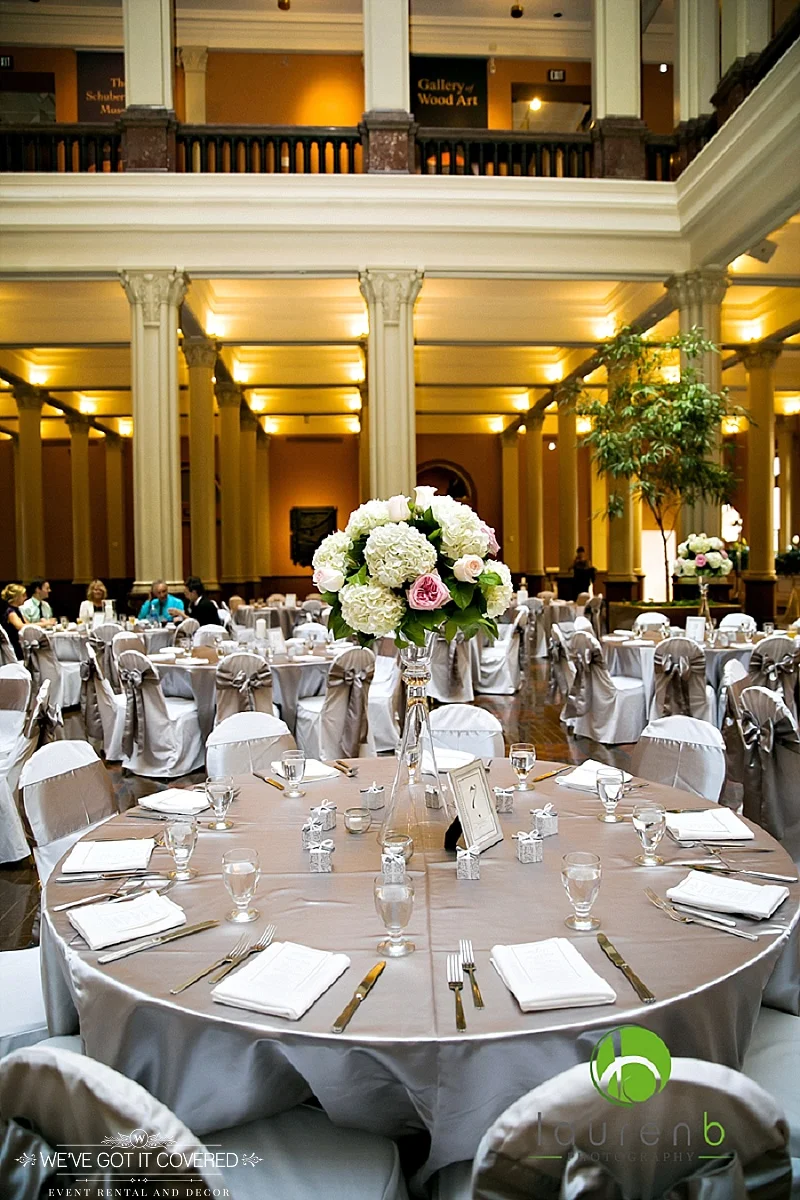Silver satin table cloths with satin sashes and white chair covers styled at the landmark center