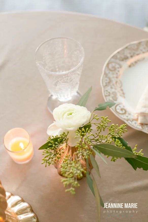 White flower in a mercury glass bud vase on a champagne linen with a candle nearby
