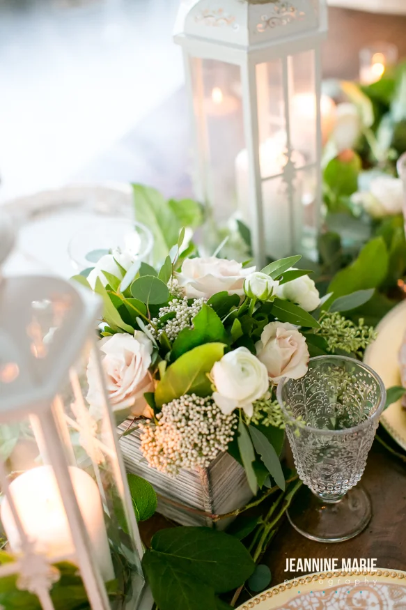 Lanterns with candles inside displayed near a floral wood box and crystal glasses
