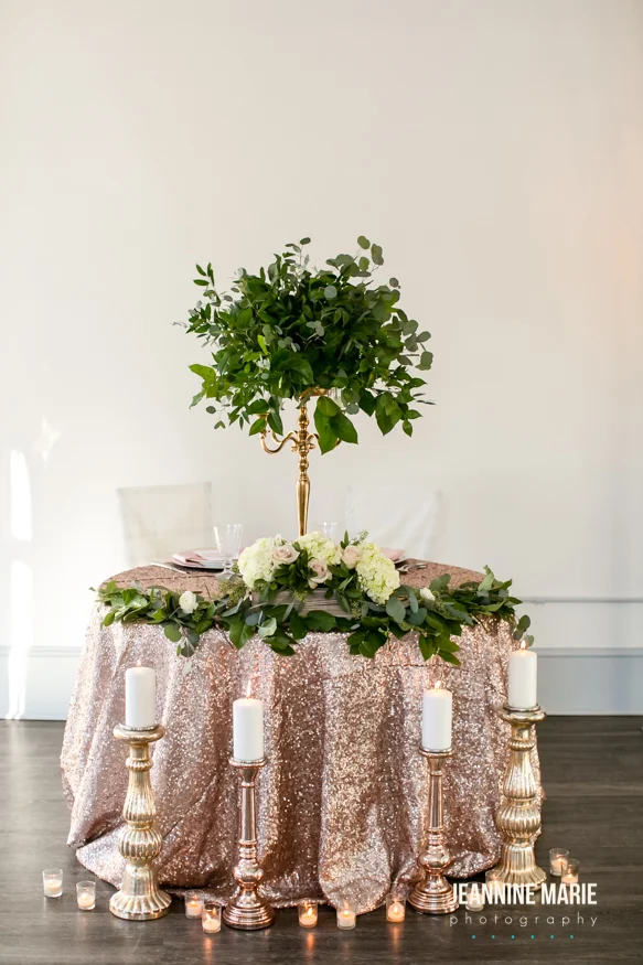 Sweetheart table with gold candelabra holding greenery arrangement. Romantic candles placed nearby.