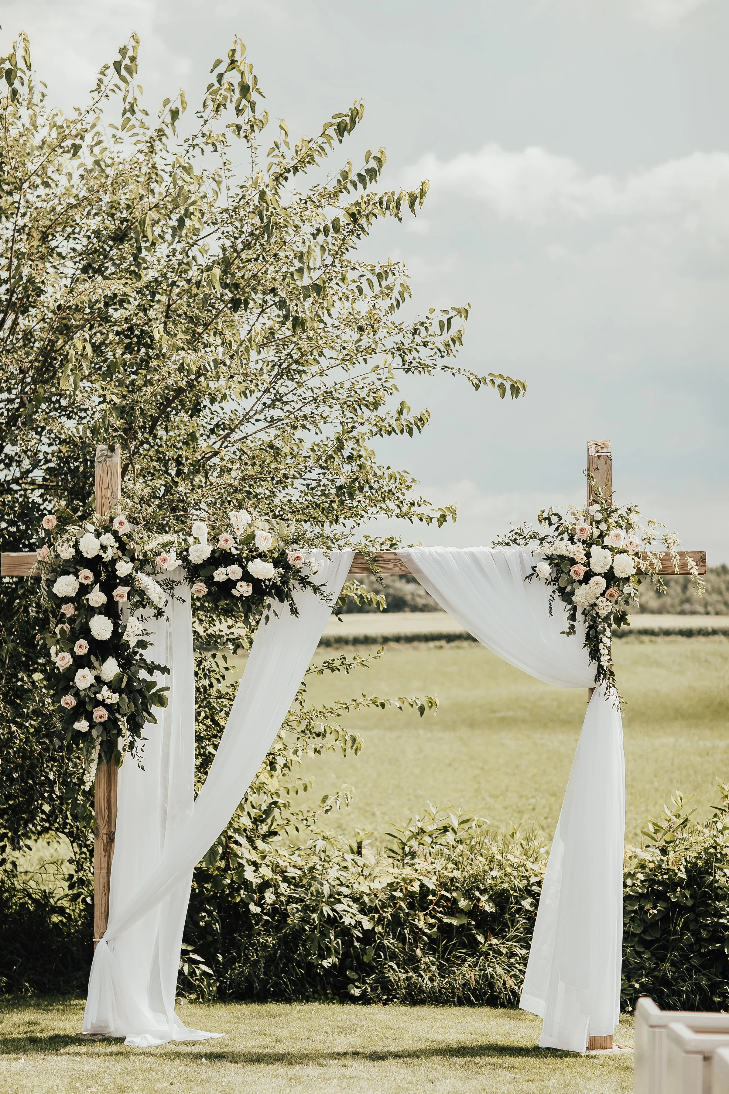 Summer wedding with draping on the ceremony arch and flower arrangements attached