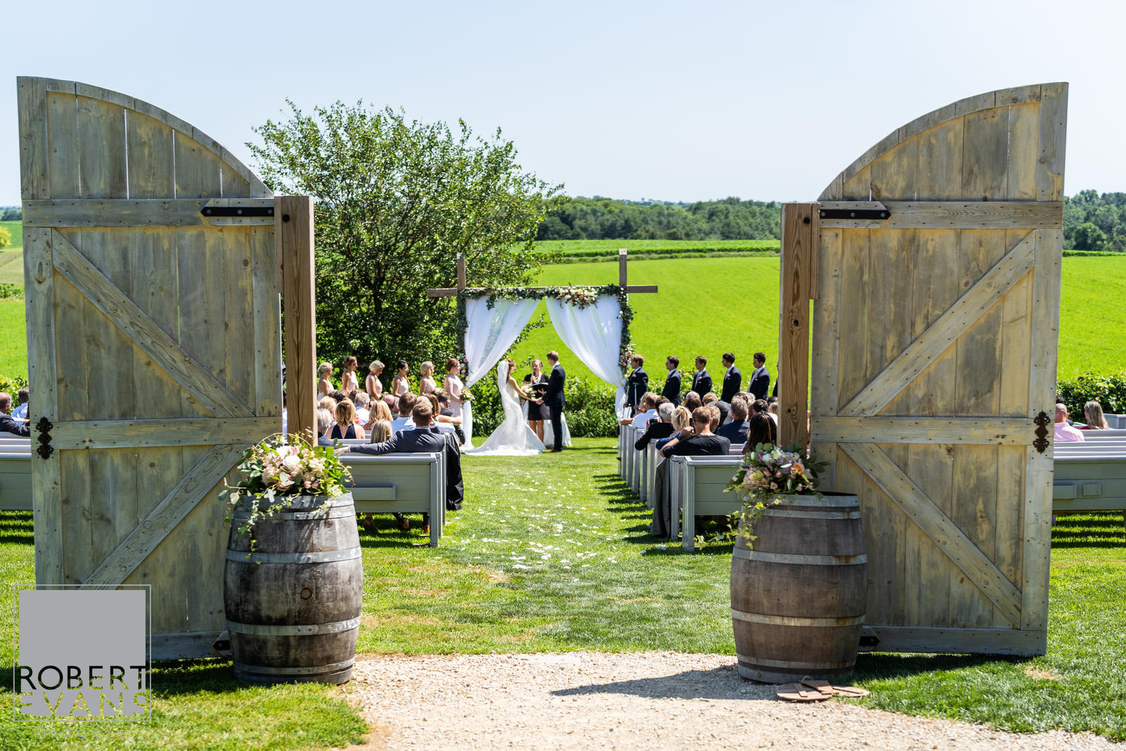 Ceremony arch decorated with white curtains pulled back and greenery to frame