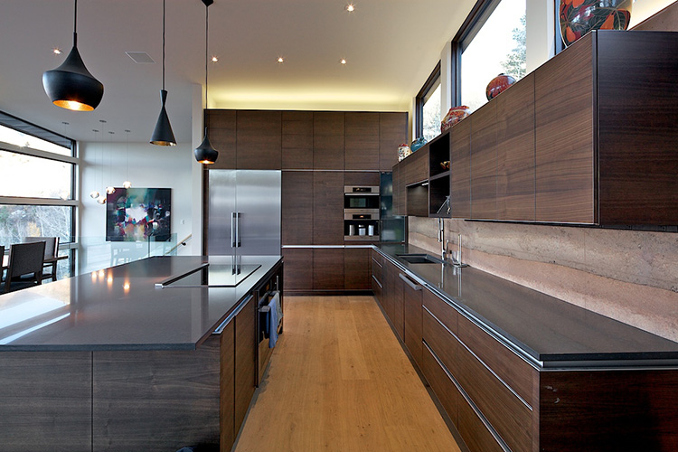  Sleek modern L-shaped kitchen with tall dark cabinetry and deep gray countertops and large center island 