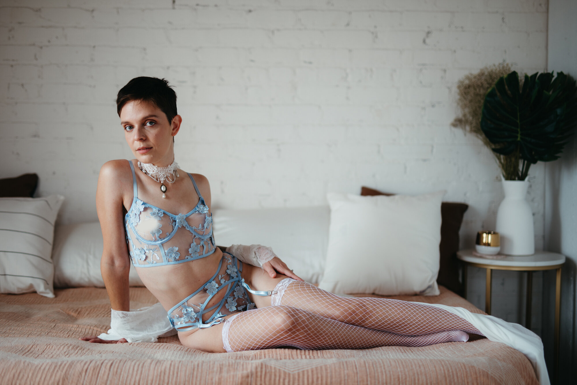Genderqueer person wearing victorian style lingerie set laying sideways on a bed