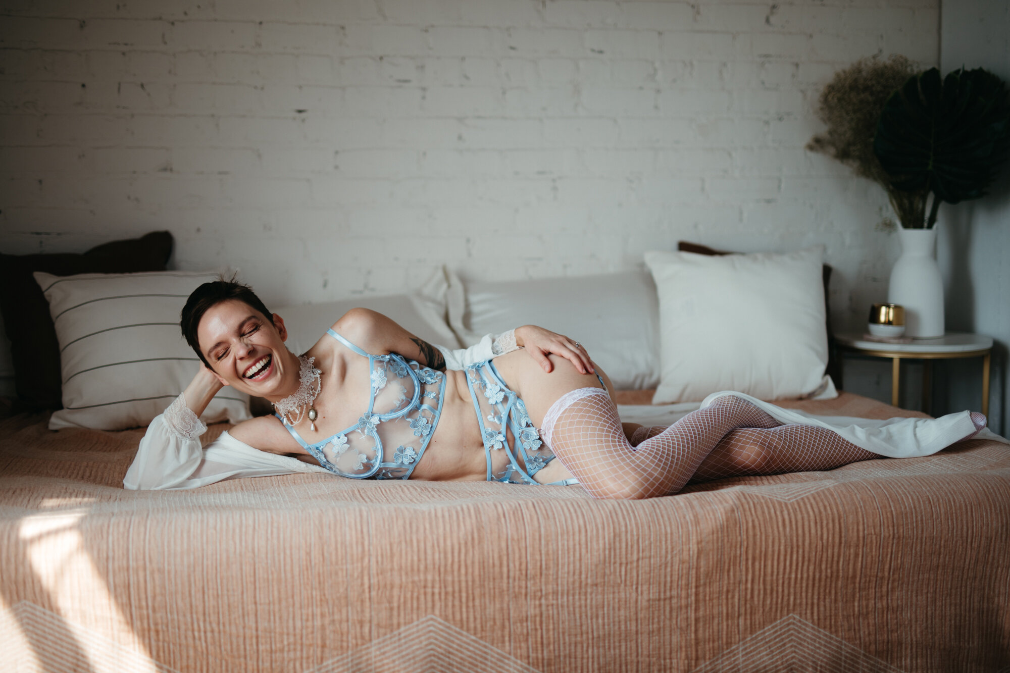 Genderqueer person wearing victorian style blue lingerie laying on a bed and laughing