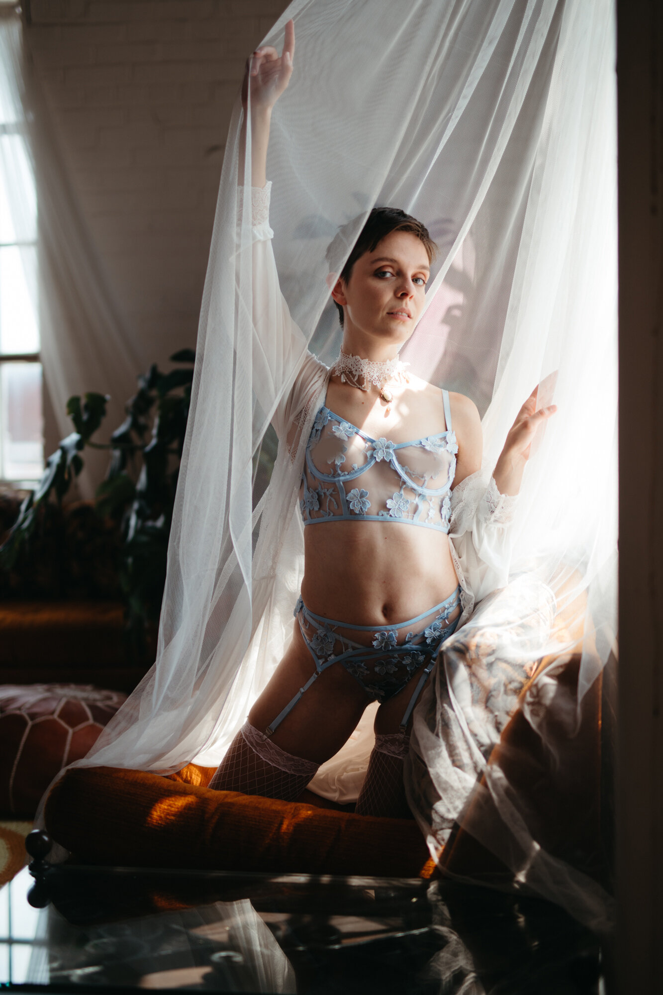 Queer boudoir photo of person with short hair in lingerie set draped in sheer fabric