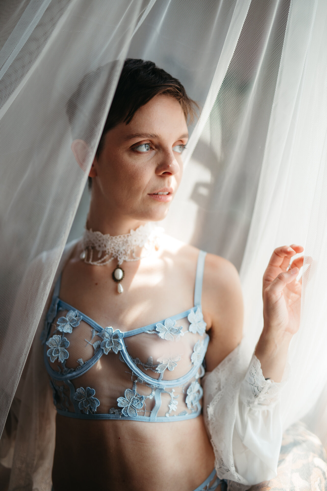 Boudoir photo of a person with short brown hair looking out of a window