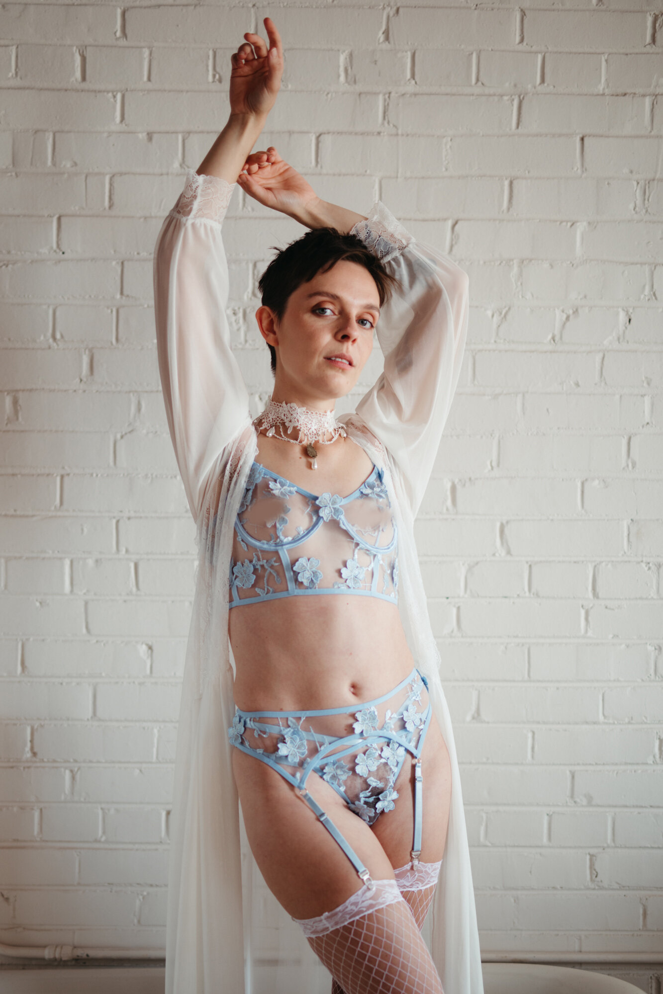 Genderqueer person wearing victorian style blue lingerie and a white robe reaching upwards