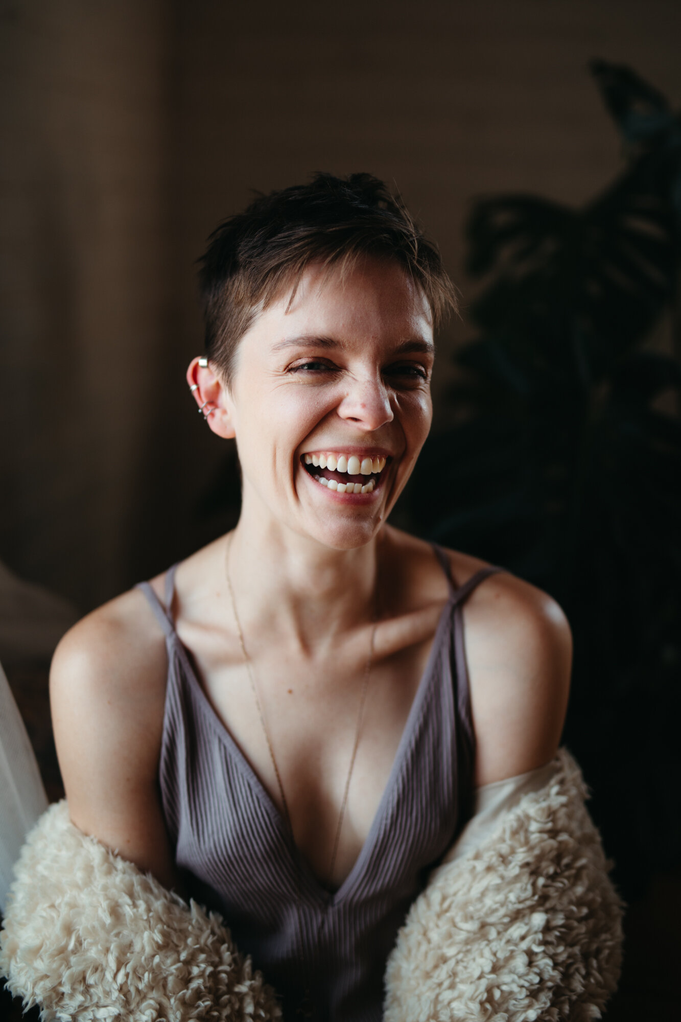 Queer boudoir photo of person with short hair laughing into the camera