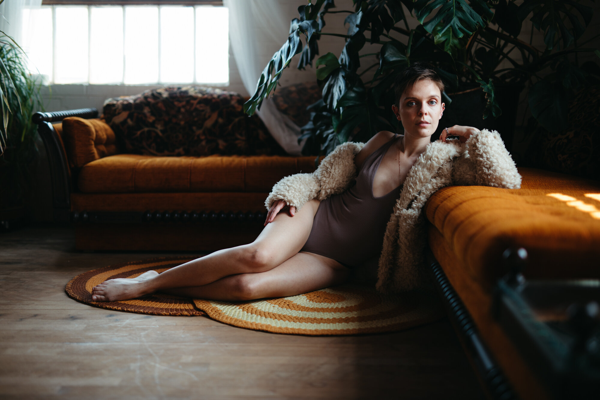 70's style queer boudoir photo of person draped over a vintage orange couch wearing a fuzzy coat