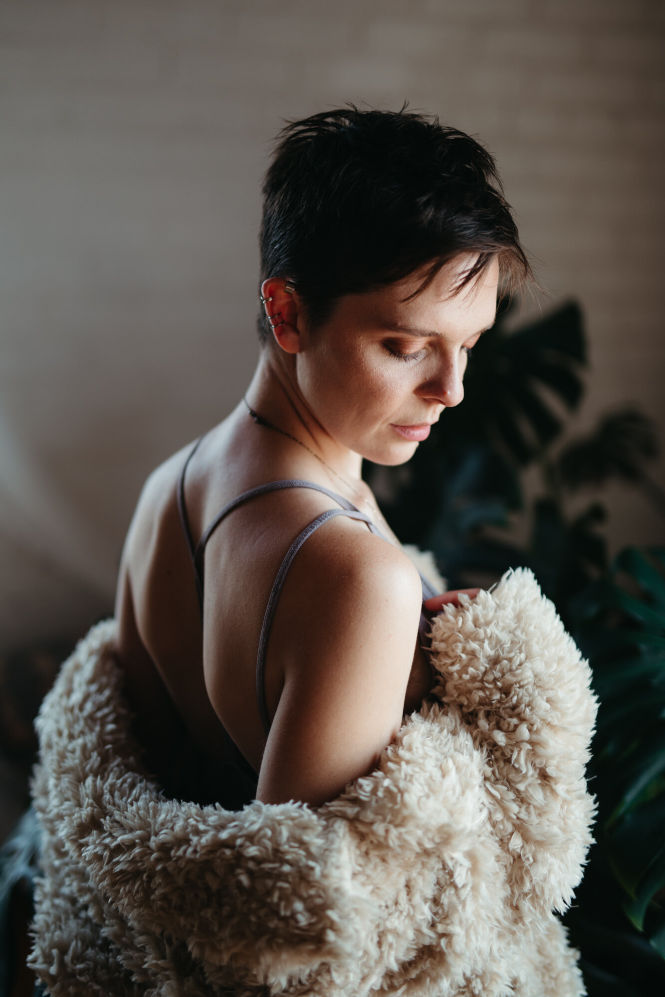 Person with short brown hair looks down with fuzzy coat sliding off their back exposing their shoulders