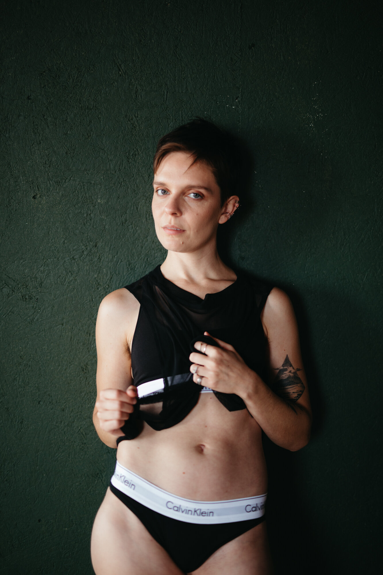 Genderqueer boudoir photo of person in mesh shirt and CK set showing off their stomach