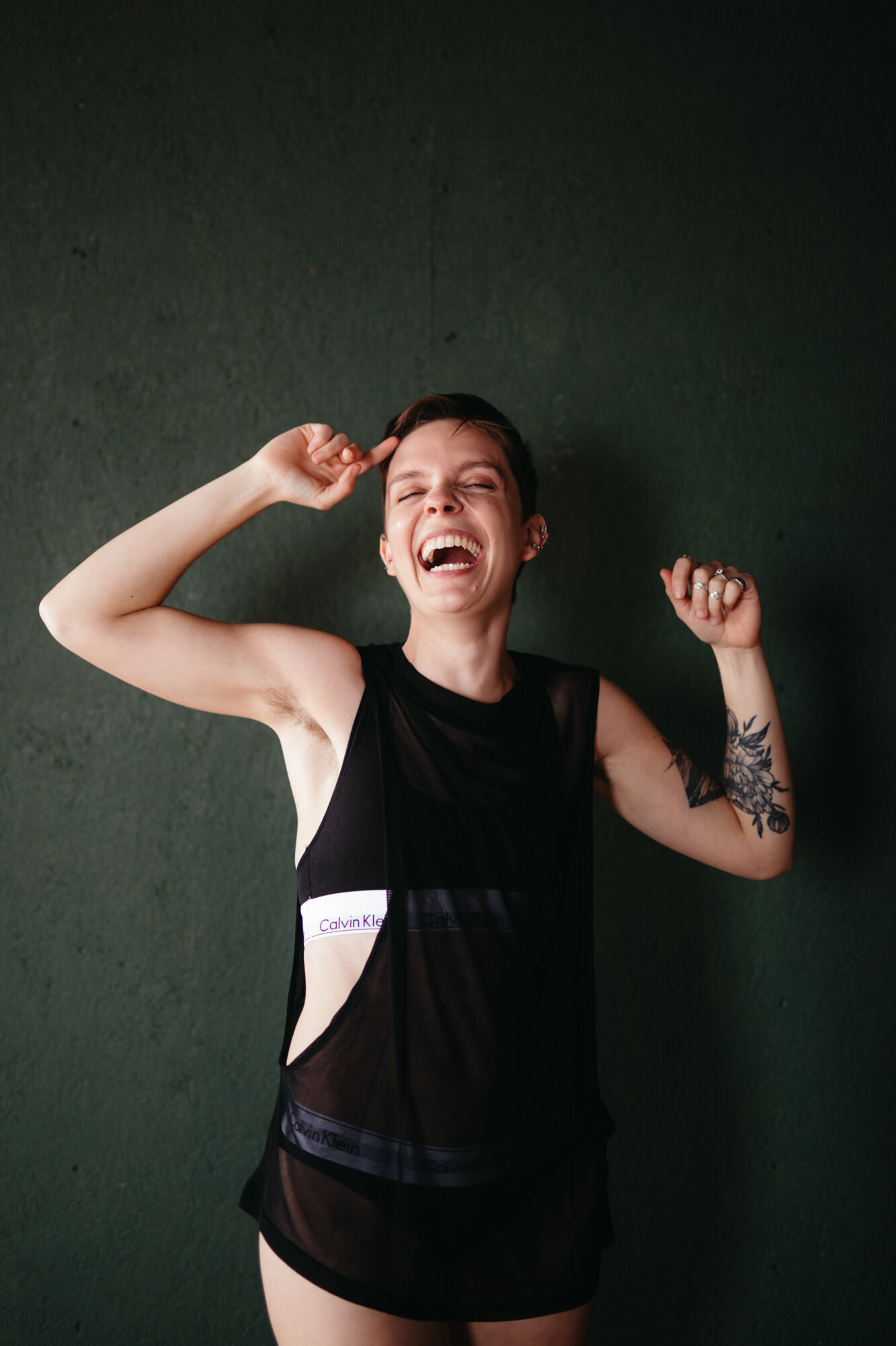 Queer masculine boudoir of person showing off their arm muscles and laughing