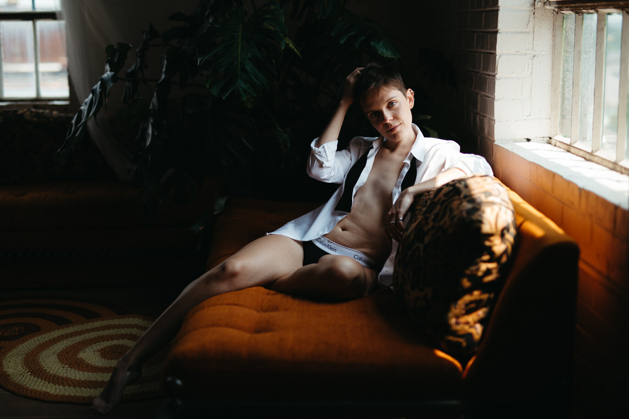 Genderqueer person in masculine attire with shirt unbuttoned and no pants, laying on couch