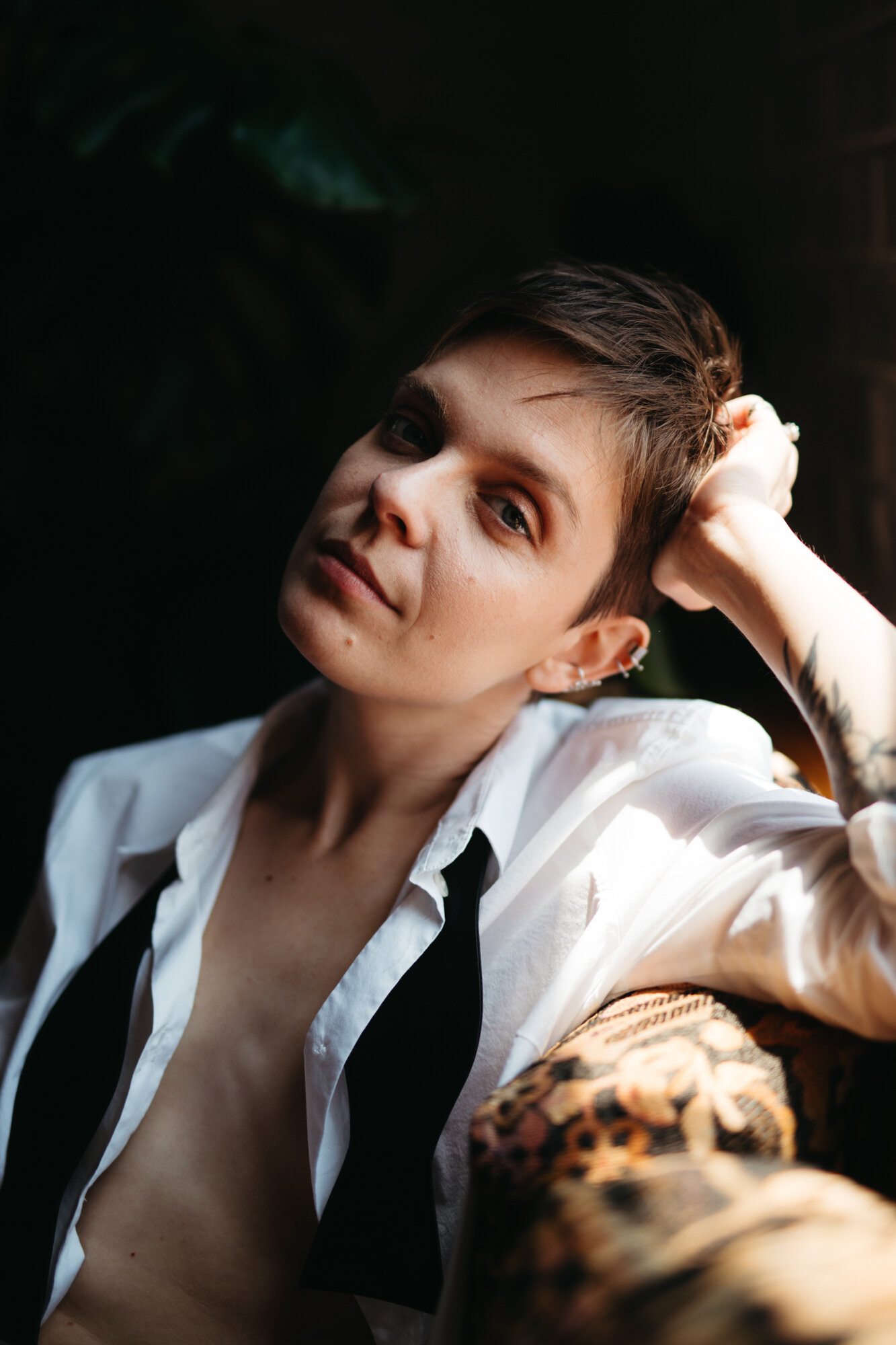 Genderqueer person in masculine outfit with shirt unbuttoned staring into camera