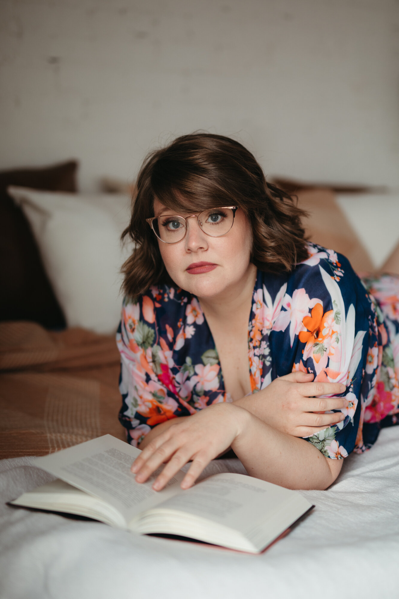 Agender person laying on bed reading book in floral robe