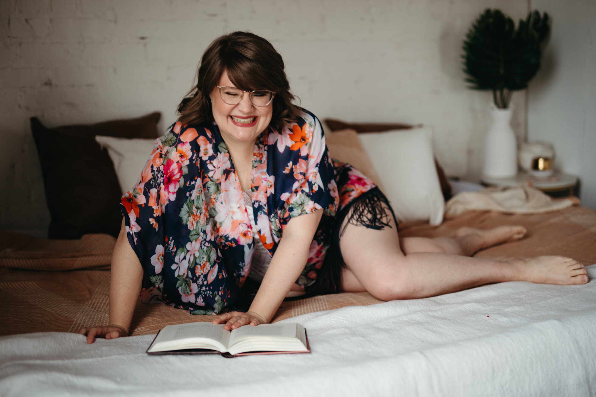 agender person laying on their side on bed with book laughing 