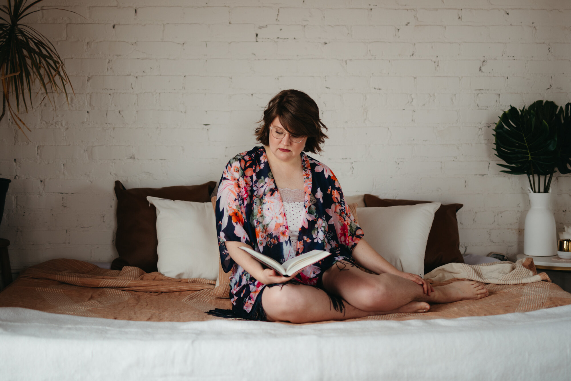 agender person sitting on bed looking down reading book