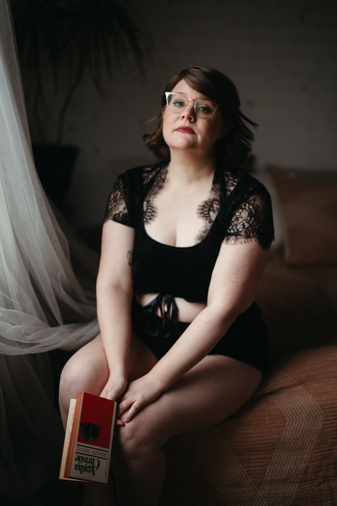 Boudoir photo of person sitting on bed with book in their hands